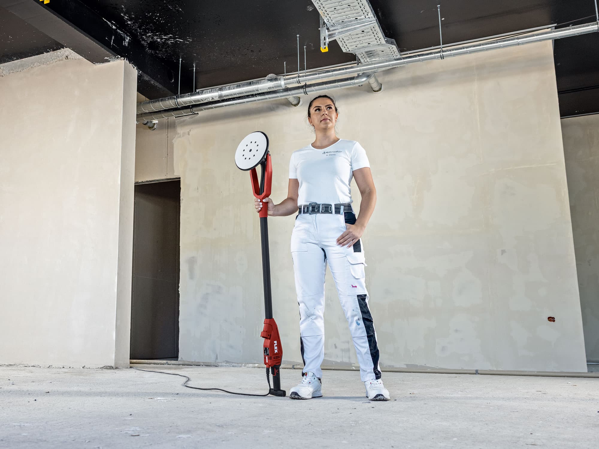 Mästarmålaren Nina står tryggt på byggarbetsplatsen med den nya FLEX GE 6 X med excentrisk drivning – en vägg- och takslipmaskin – i handen.