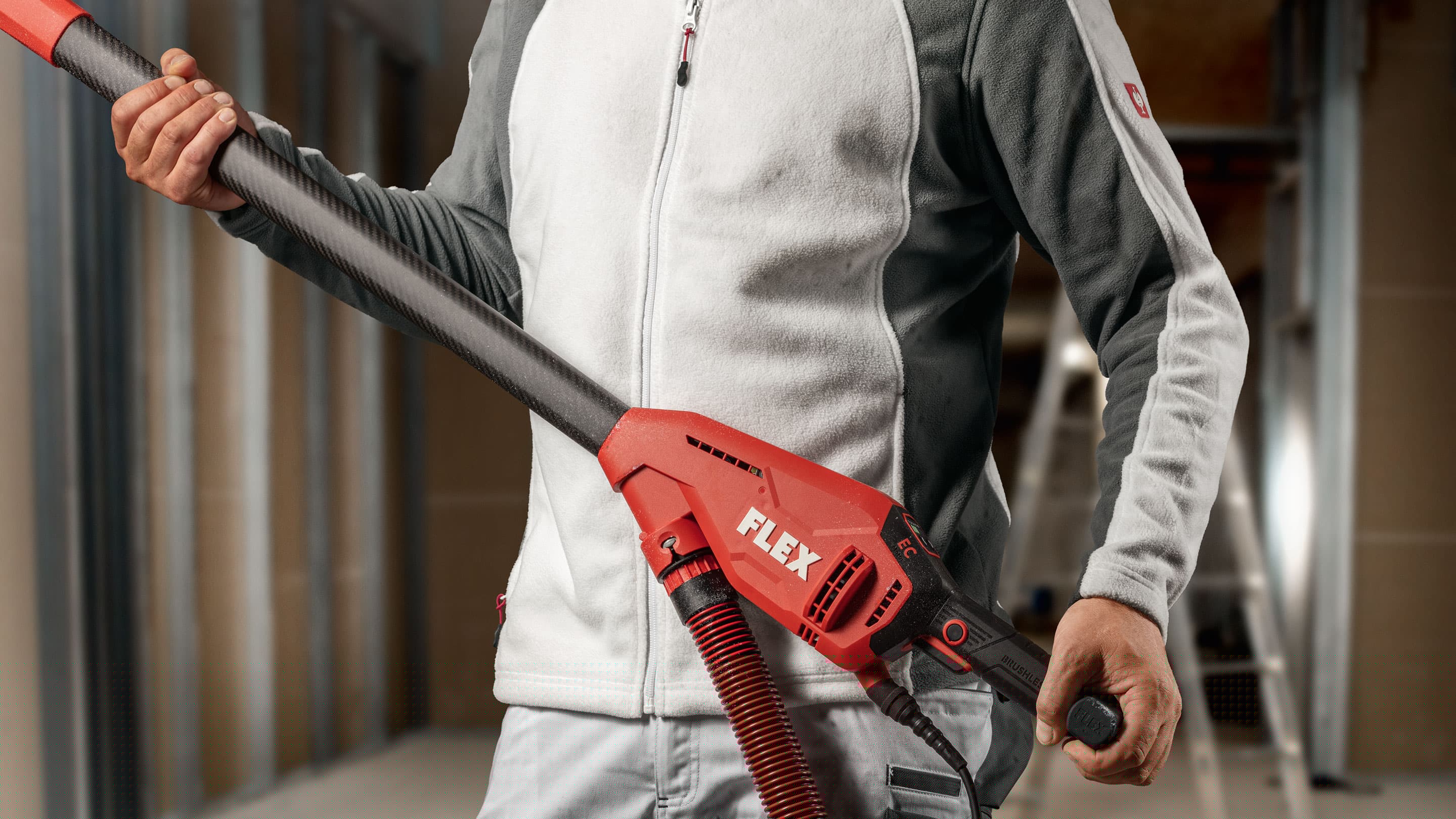 Hantverkare som håller FLEX GE 6 – den lätta slipgiraffen i kolfiber – med ergonomiskt grepp och ansluten sugslang på en byggarbetsplats.